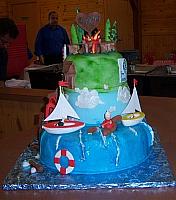 Main front view of the summer camp cake with sailboats, kayaker, and camp fire on top tier.  ALL DECORATIONS are handmade out of gumpaste(called sugarpaste in Europe) and edible.